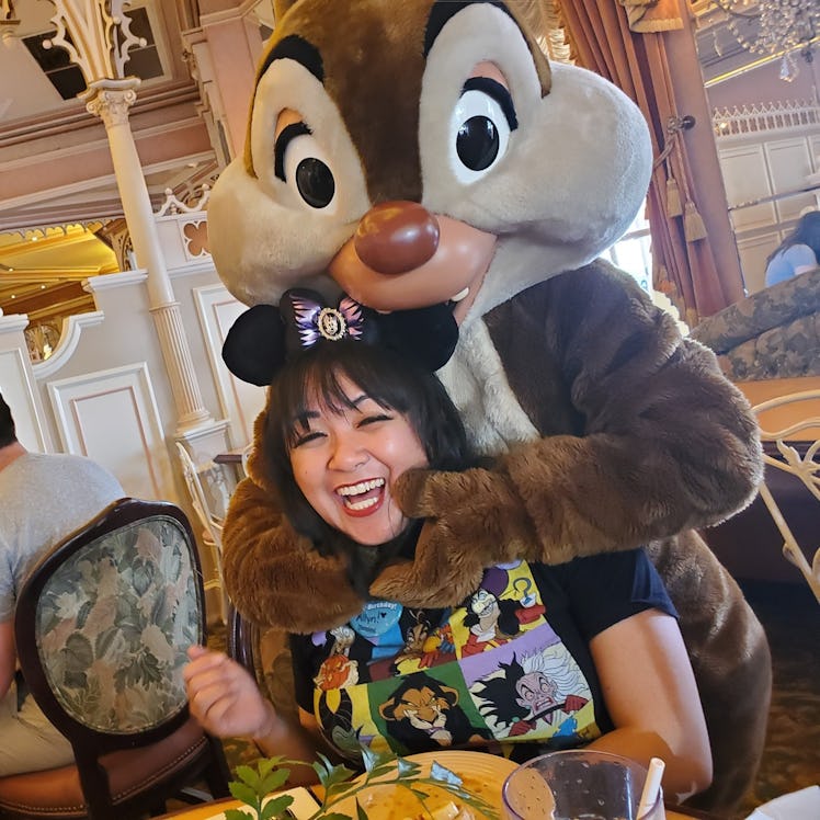 A woman wearing Mickey Mouse ears smiles with Dale at a Disneyland character breakfast. 