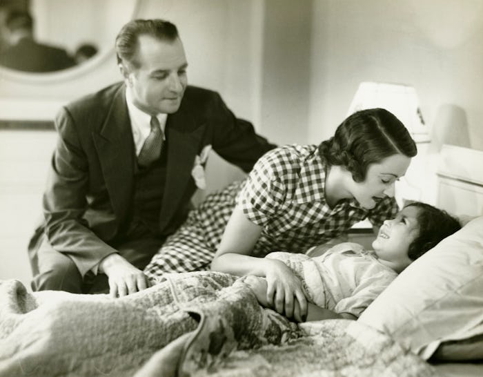 vintage picture of a mom kissing a child in bed.