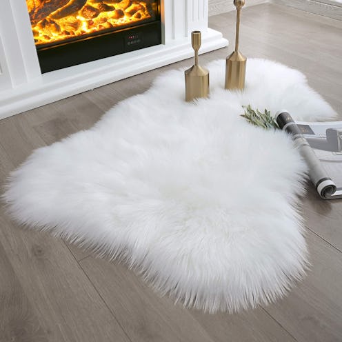 Gold candle holders sitting on a white faux fur rug, placed in front of a fire.