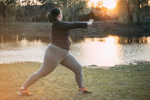 A person wearing a black shirt, grey leggins, and orange-laced sneakers leans into a yoga pose on so...