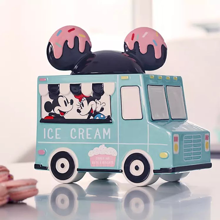 A Mickey and Minnie Mouse cookie jar shaped like an ice cream truck sits on a white kitchen counter....