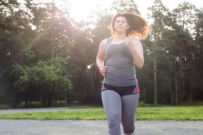 A person with her hair down and a tank top with shorts over leggings runs in a park. You can stretch...