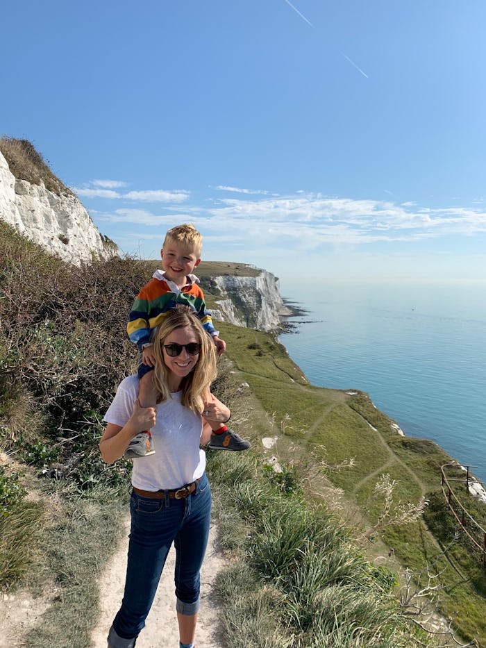 A mother stands with baby on shoulders by a cliff