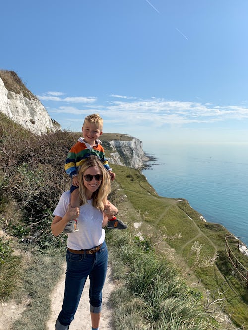 A mother stands with baby on shoulders by a cliff