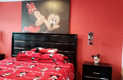 This Mickey Mouse-themed Airbnb has a Mickey-themed bedroom with red bedding, red walls, and a portr...