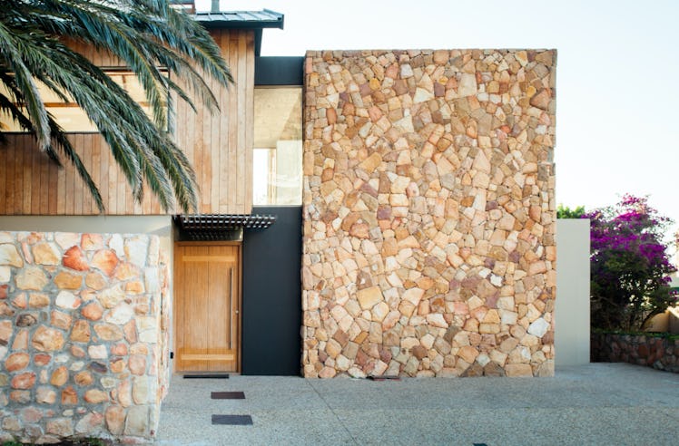 A charming studio in Cape Town, South Africa has a stone and black exterior and a giant palm tree ne...