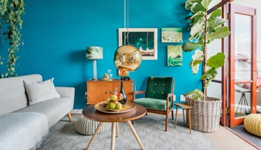 The living room of a colorful apartment in Cape Town, South Africa has a bright blue wall and mid-ce...