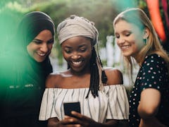 Three friends with headscarves looking at phone, taking selfie