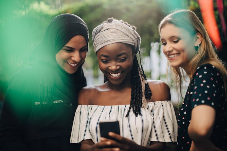 Three friends with headscarves looking at phone, taking selfie