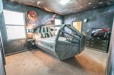 A spaceship bed sits in the center of a 'Star Wars'-themed Airbnb bedroom with galaxy painted walls....