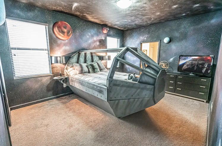 A spaceship bed sits in the center of a 'Star Wars'-themed Airbnb bedroom with galaxy painted walls....