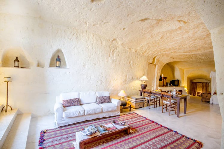 A living room in a cave home on Airbnb has a bright red and purple rug with a white couch. 
