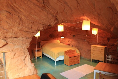 A bedroom in a cave home on Airbnb has a bed, wood furniture, and hanging lanterns.