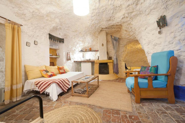 The living room in a cave home in Spain on Airbnb has a blue chair and daybed futon. 