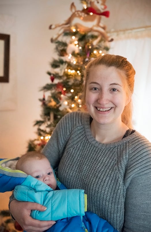 A mother holds her child in front of a Christmas tree