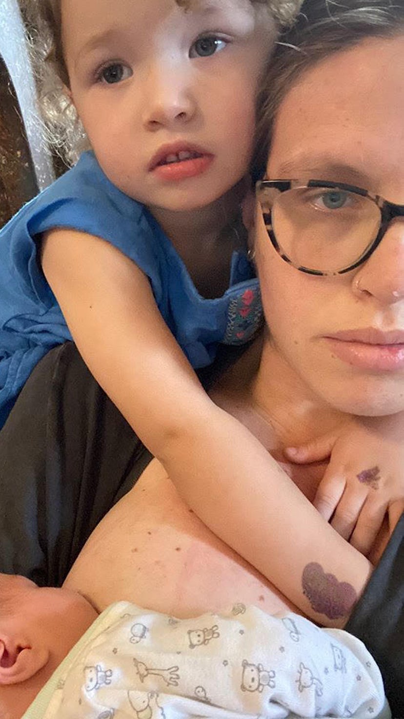 A mother nurses her baby while her toddler hugs her from behind and puts his hand down her top