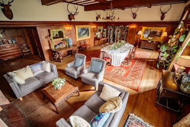 The living room in the castle listed on Airbnb has animals on the wall, a large dining table, and pl...