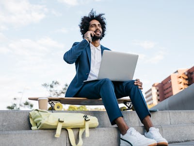 A man sitting on a skate board and holding a laptop on his lap