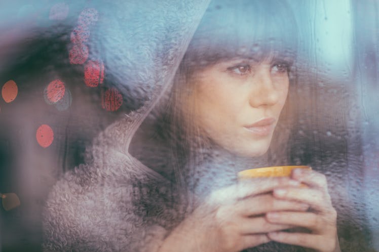 Young woman with coffee looking out window during rain
