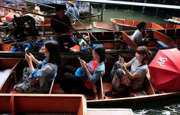 Tourists looking at their mobile phones instead of the passing sights at the famous Damnoen Saduak F...