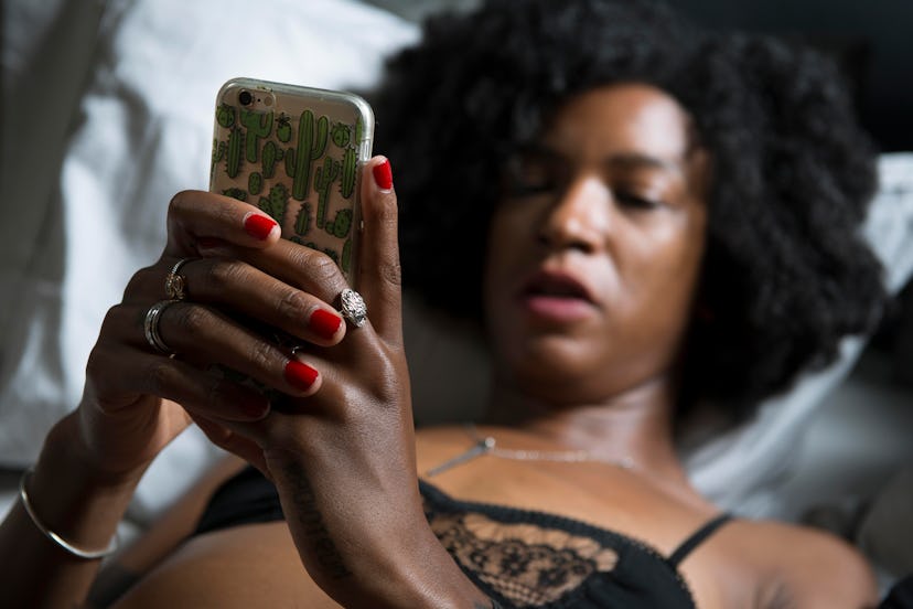 A woman in lingerie looks at her phone. Sexting can trigger the body's limbic system.