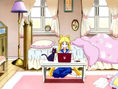 Sailor Moon sits in her iconic cartoon bedroom and types on her pink laptop with her cat, Luna, near...