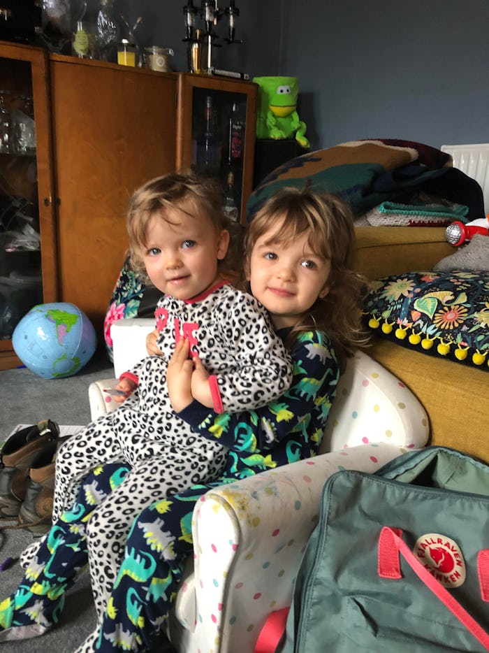 Two toddlers sit one on the other in a chair