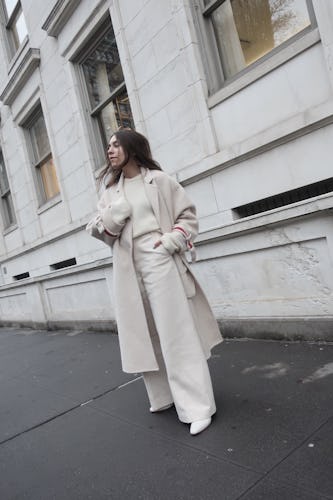 Lauren Caruso standing on a street in a white coat, white pants, and white heels