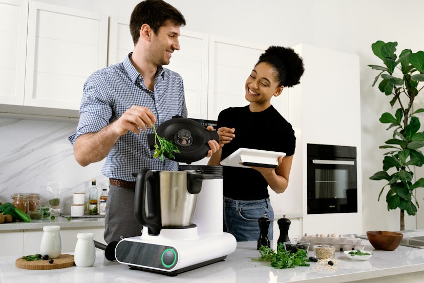 An image of a food processing cooking robot flanked by two humans who are cooking. 
