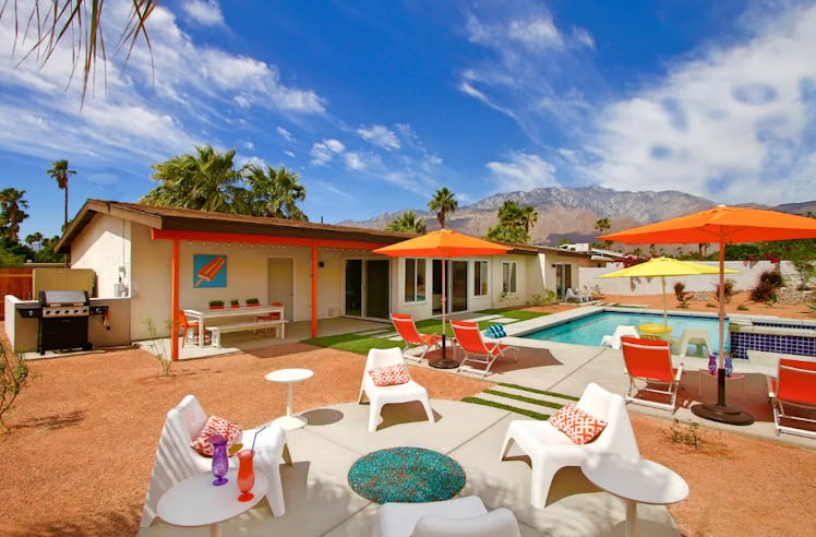 A backyard pool area in Palm Springs has orange lounge chairs and umbrellas. 