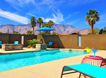 A pool with bright blue lounge chairs has mountains in the background in Palm Springs.