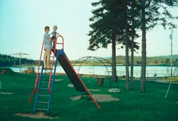 A mother standing at the top of a slide with her young son.