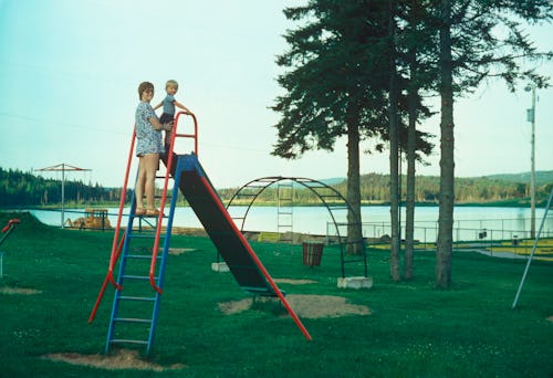 A mother standing at the top of a slide with her young son.
