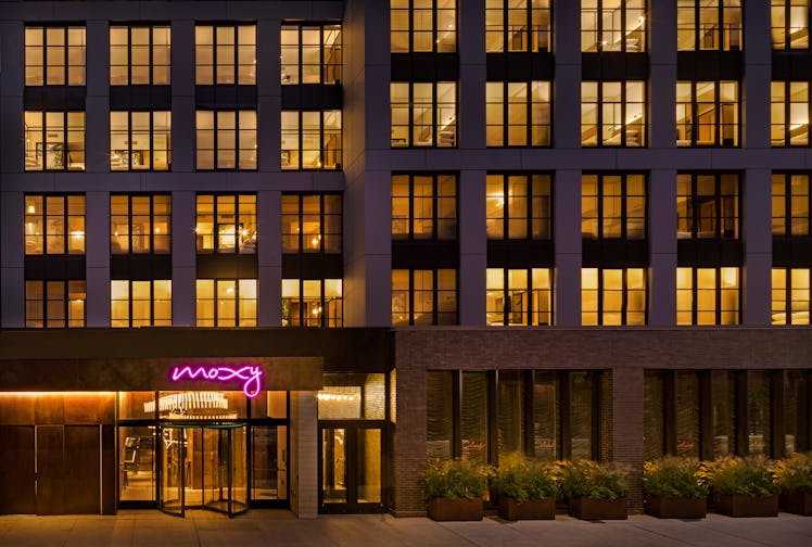 The exterior of the Moxy East Village has a neon pink sign and greenery.