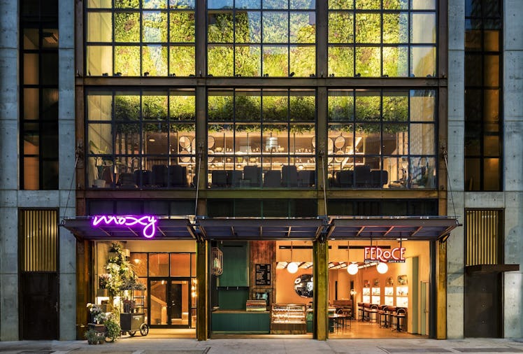 The exterior of Moxy Chelsea at night features neon lights and looks into its chic interior.