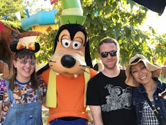 A group of friends poses for a picture with Goofy at Disneyland. 