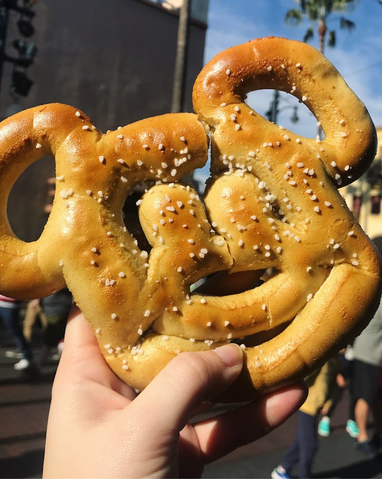 A woman holds up her Mickey-shaped pretzel at Disneyland. 