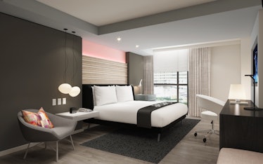 A guest room at Hotel Zena has modern decor, a view of the city, and a light pink accent wall. 