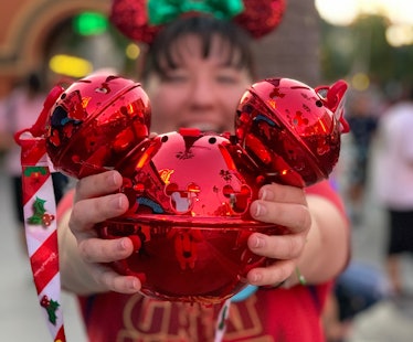 A woman holds out her shiny red Mickey-shaped popcorn bucket she bought at Disneyland.