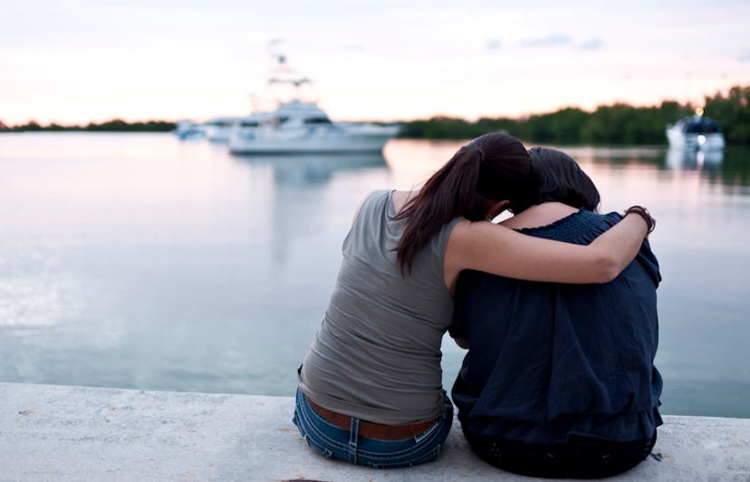 woman comforting her friend  while sitting next to a body of water