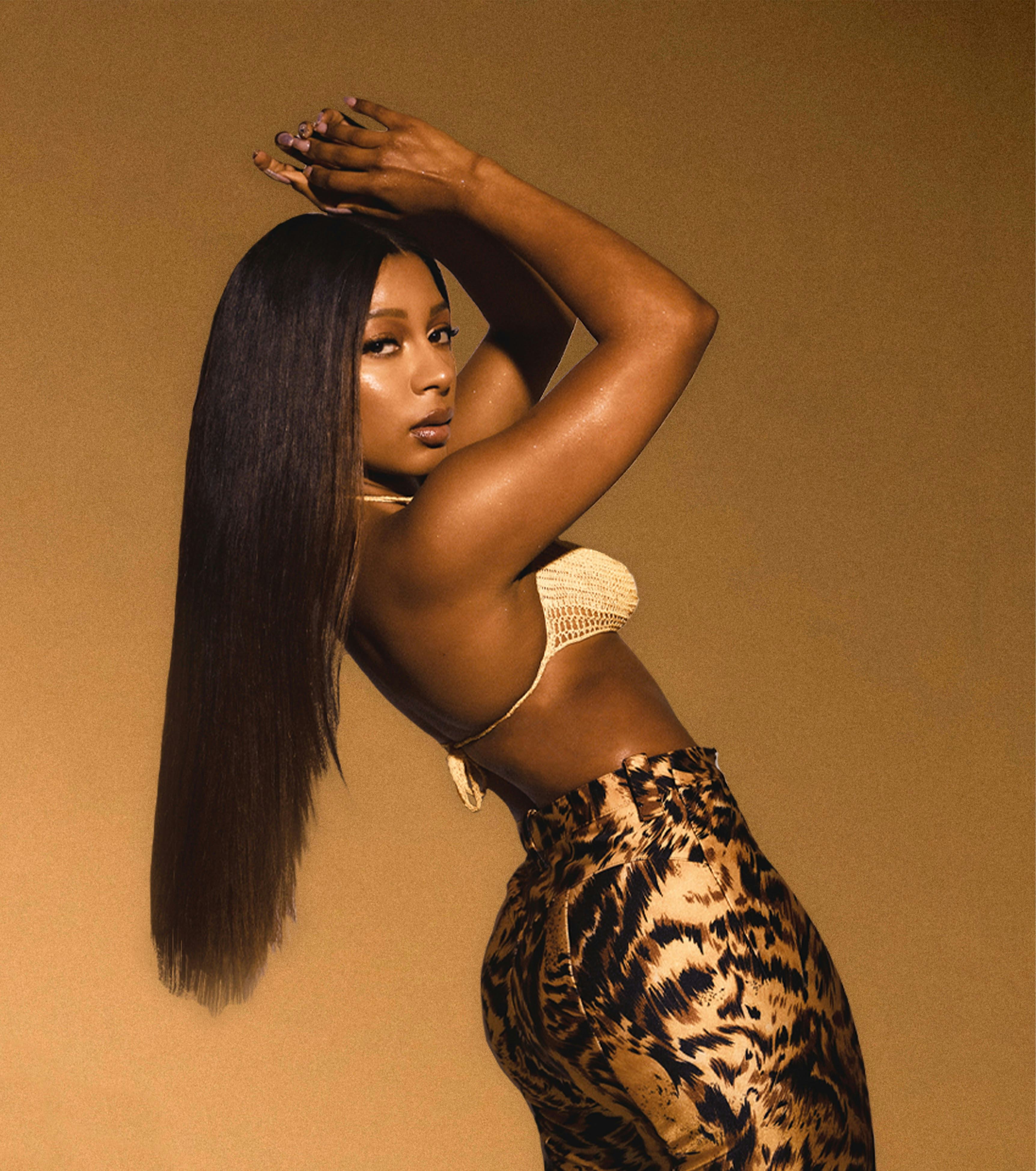 Victoria Monét poses with her hands clasped above her head.