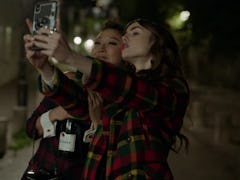 Emily (Lily Collins) and Mindy (Ashley Park) pose for a selfie in Paris at night. 