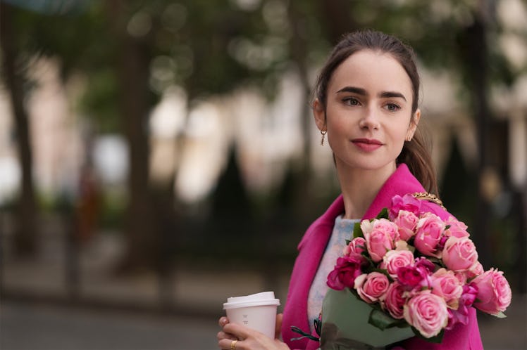 Emily from 'Emily in Paris' wears a hot pink pea coat and holds a coffee cup and bouquet of roses.