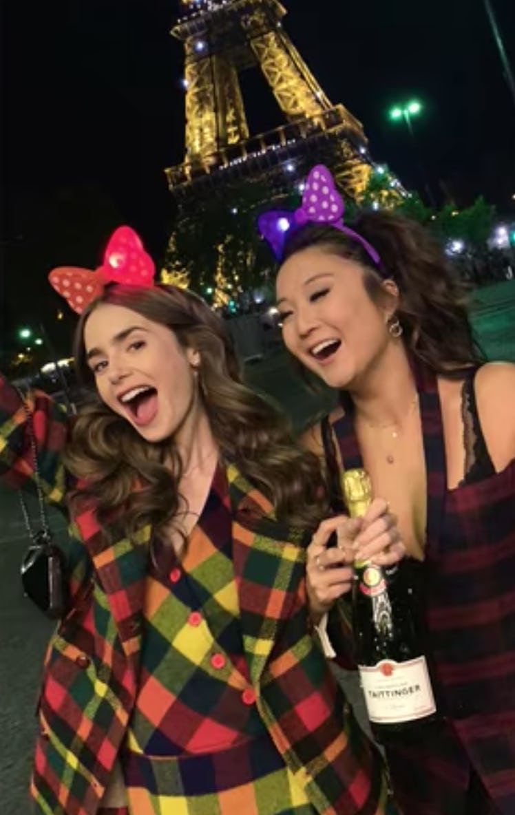 Emily (Lily Collins) and Mindy (Ashley Park) pose with a bottle of champagne in front of the Eiffel ...