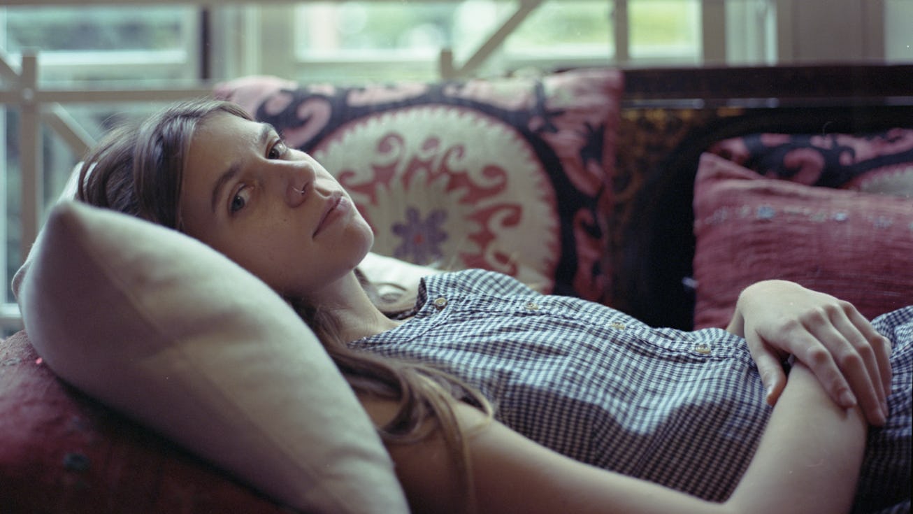 A photo Tomberlin in a checkered top laying back on a couch, looking into the camera.