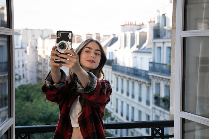 LILY COLLINS as EMILY in episode 101 of EMILY IN PARIS, shown taking a selfie on her balcony in Par...