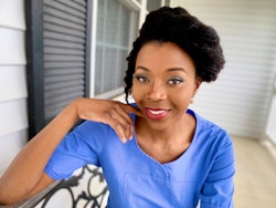 A woman in a blue top smiling while posing for a picture on the front porch of her house