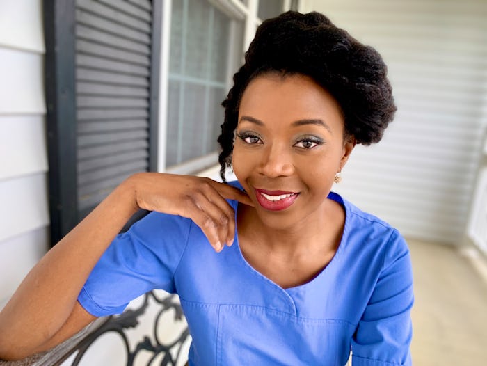 A woman in a blue top smiling while posing for a picture on the front porch of her house