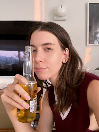 Danielle Haim in a maroon tank top holding a bottle of corona