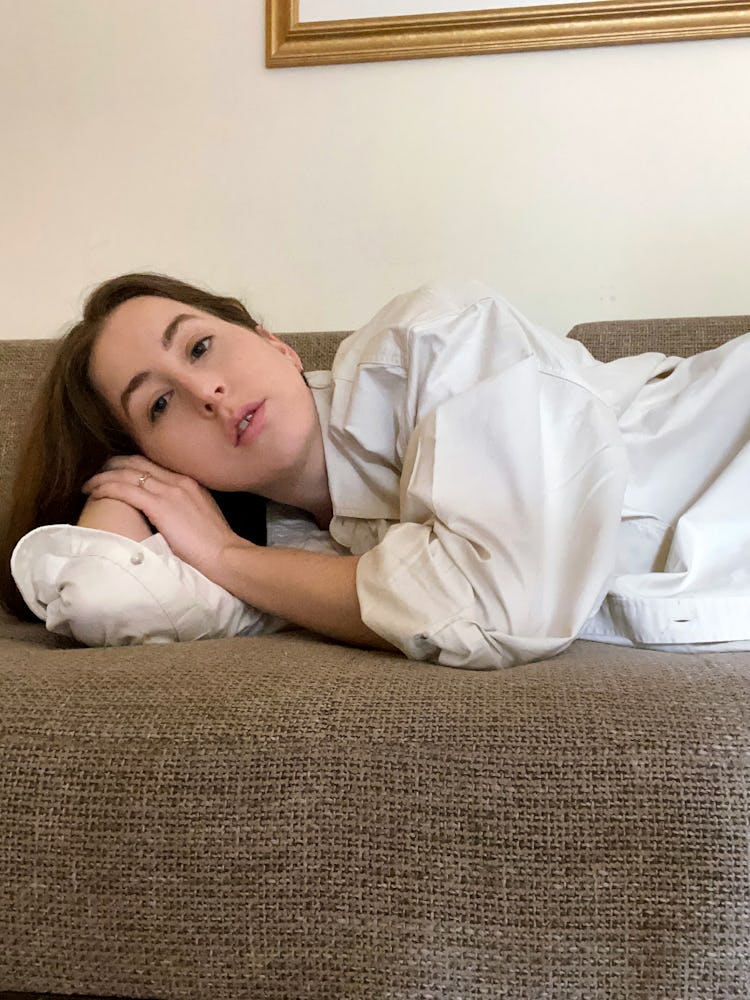 Alana Haim lying down on her side on a couch in a white button up shirt